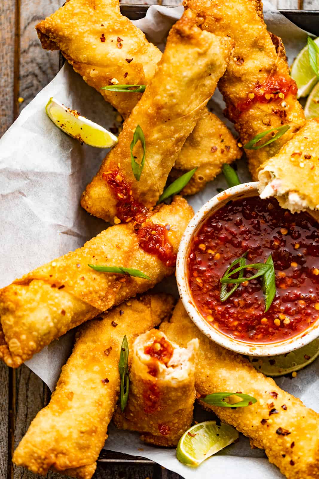 crab rangoon egg rolls in a basket with a bowl of sweet and sour dipping sauce.