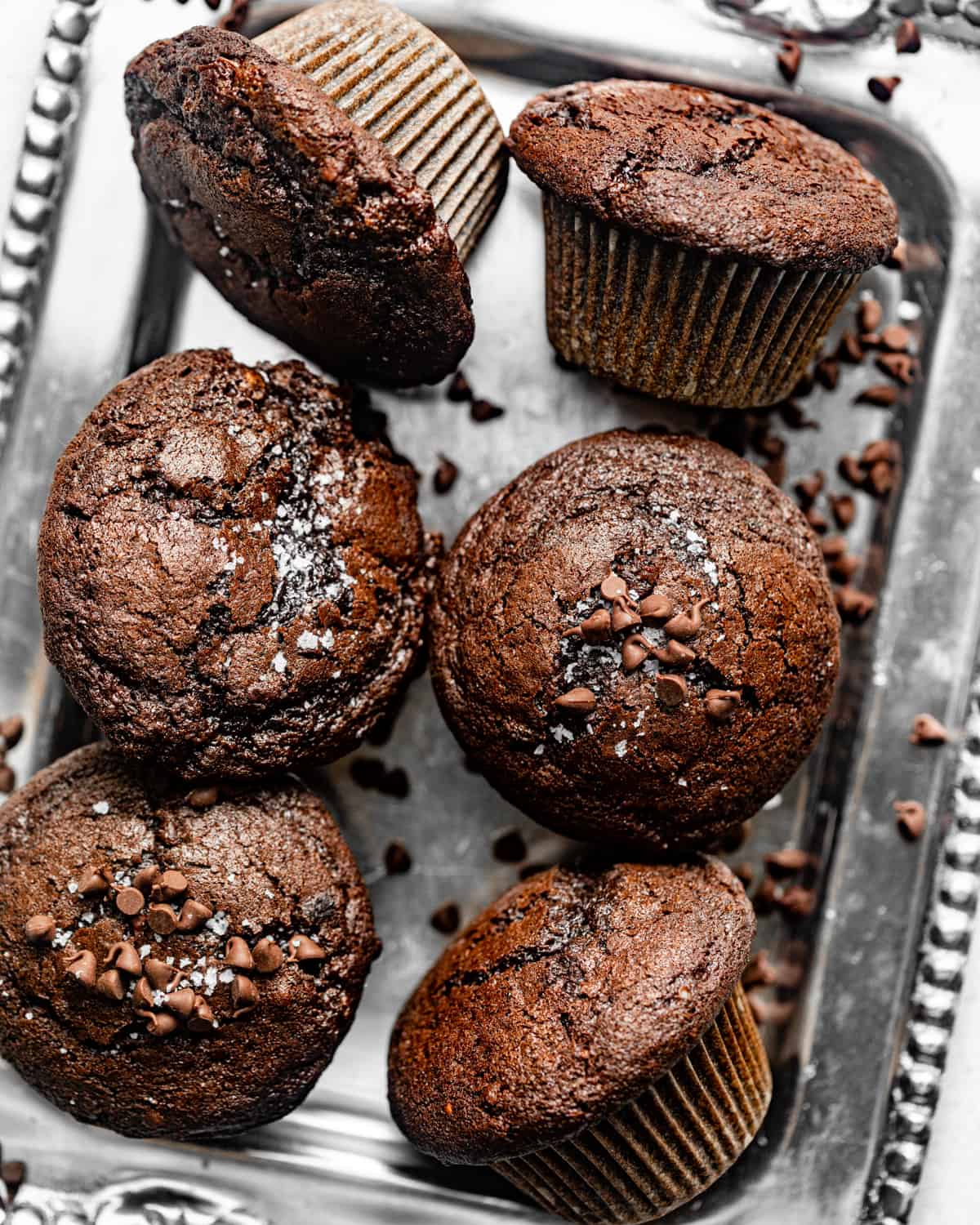 double chocolate chip muffins on a silver tray garnished with chocolate chips and flaky salt.