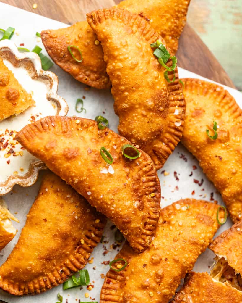 empanadas on a piece of parchment paper garnished with green onions and red pepper flakes.