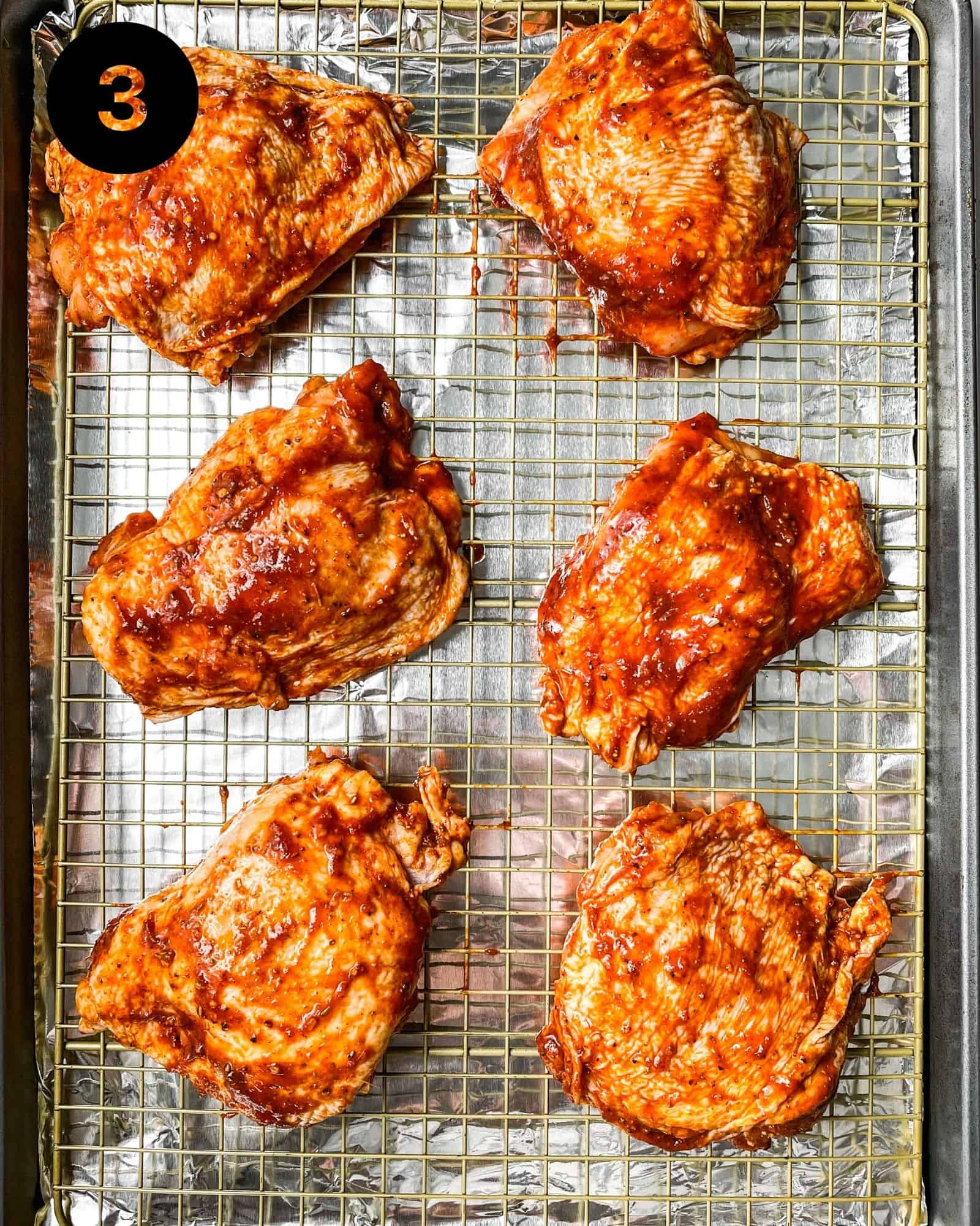 chicken thighs on a sheet pan covered in barbecue sauce.