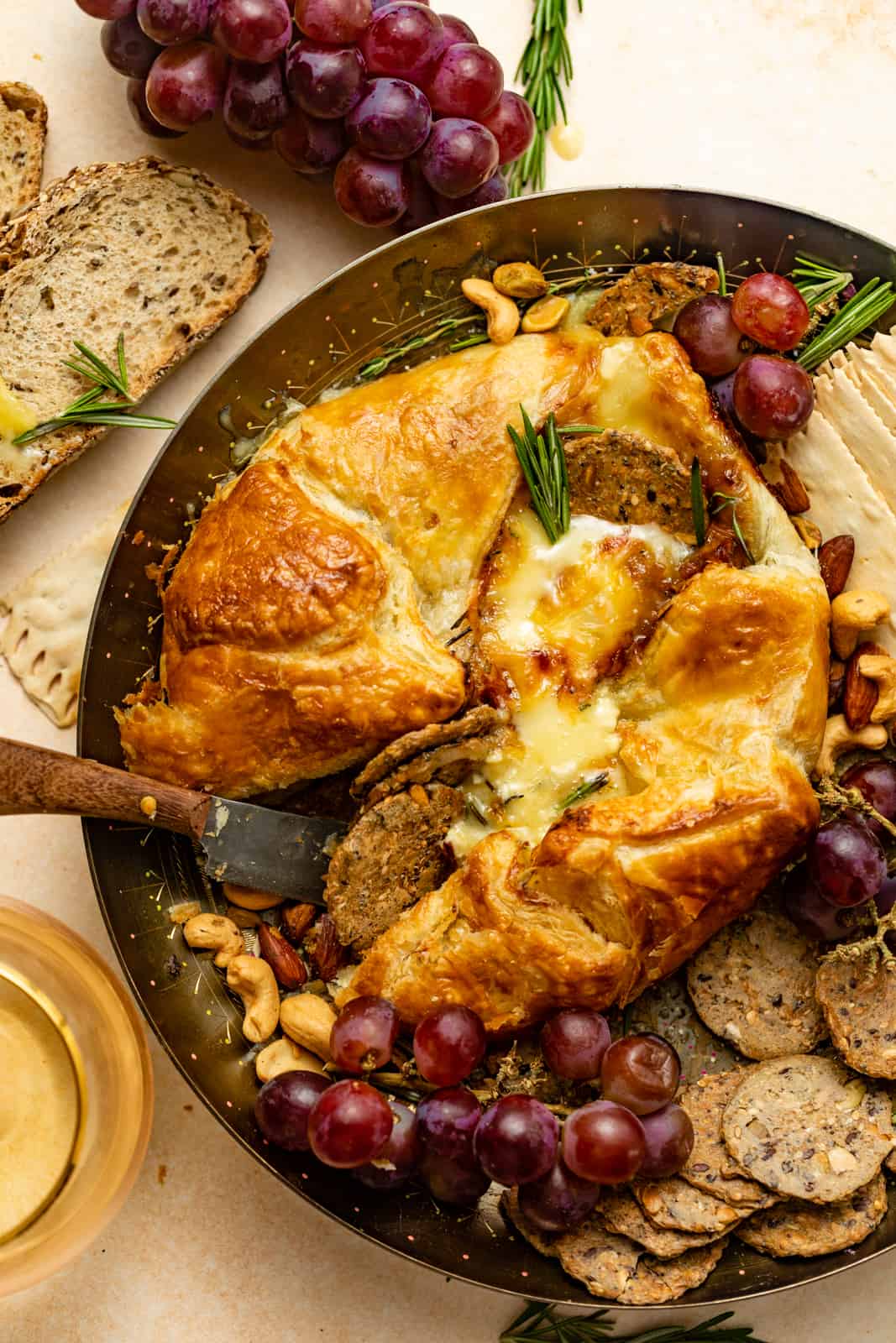baked brie in puff pastry on a gold plate with grapes and crackers.