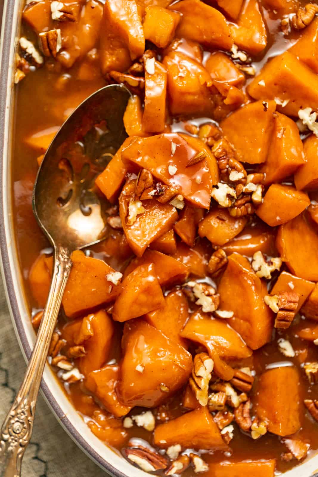 candied sweet potatoes in a casserole dish with a serving spoon.