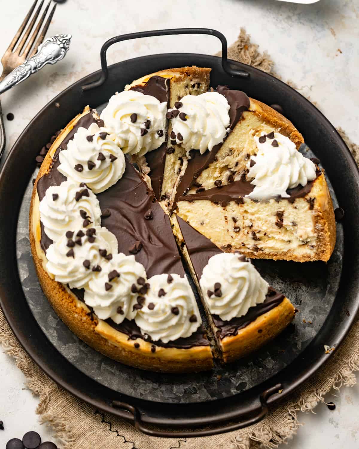 a chocolate chip cheesecake on a black serving tray with a few slices cut out of the cake.