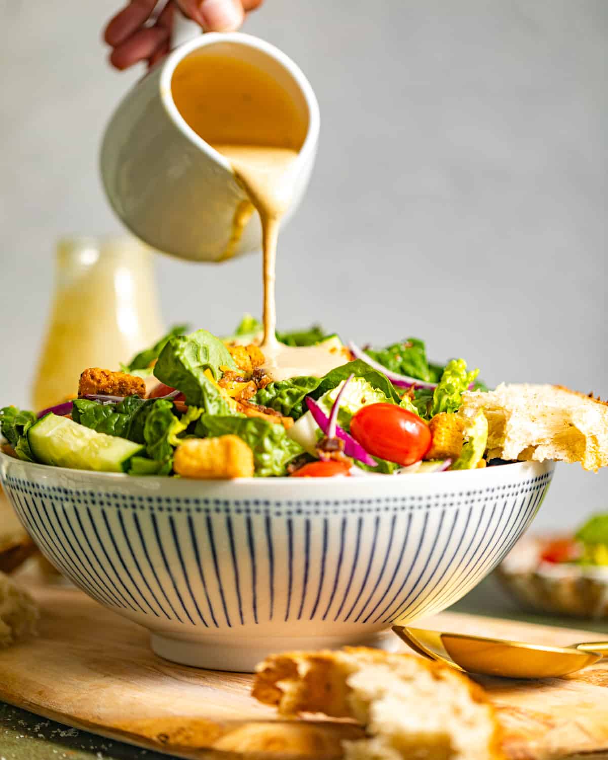 creamy balsamic dressing in a glass being poured on top of a salad in a bowl.