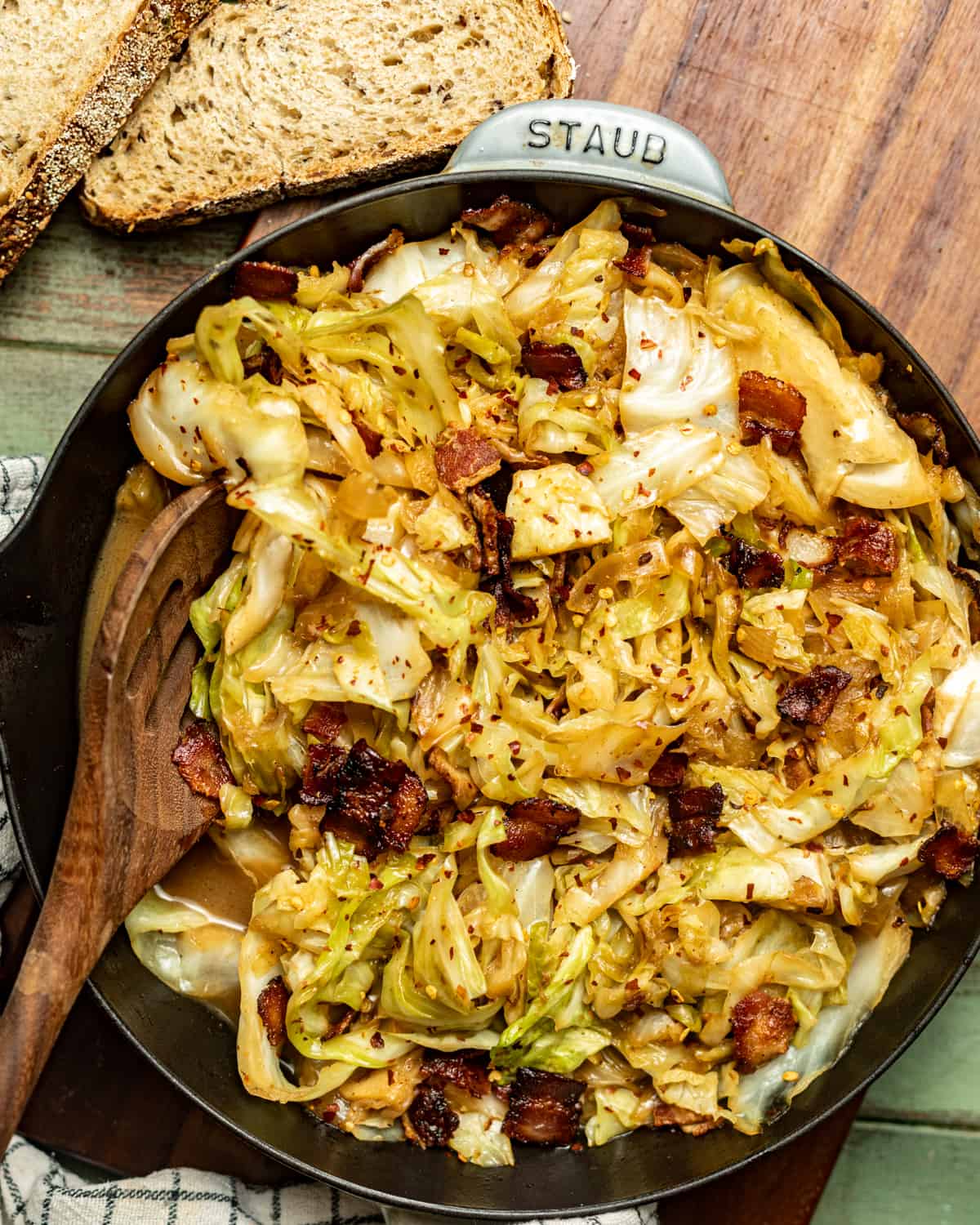 a skillet filled with fried cabbage with onions and bacon with a piece of bread on the side.