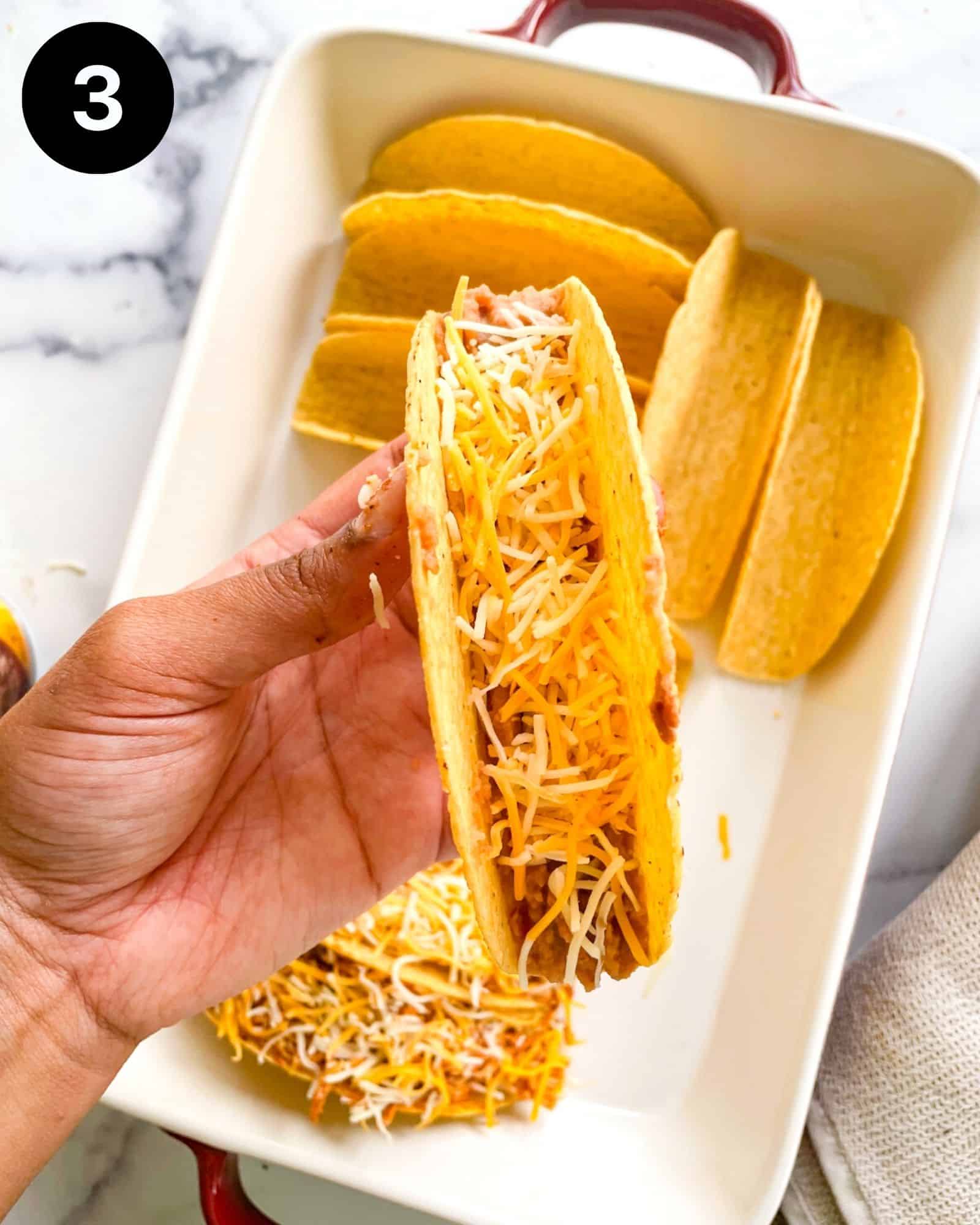 a hand holding a hard taco shell stuffed with cheese and refried beans.