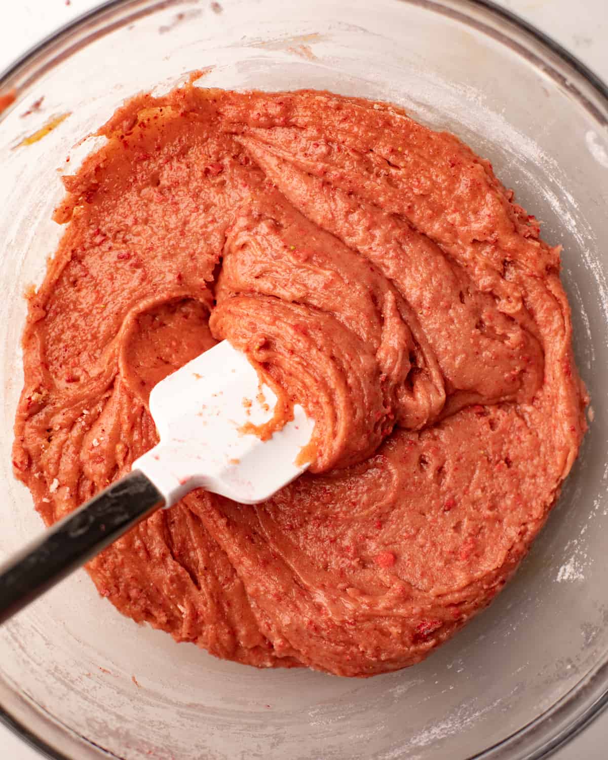 strawberry cake batter mixed together in a bowl with a flat spatula.