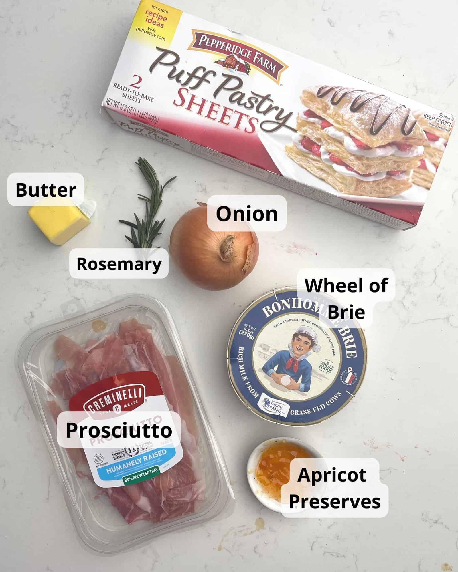 ingredients to baked brie in puff pastry - puff pastry, wheel of brie, apricot preserves, prosciutto, onion, rosemary, and butter.