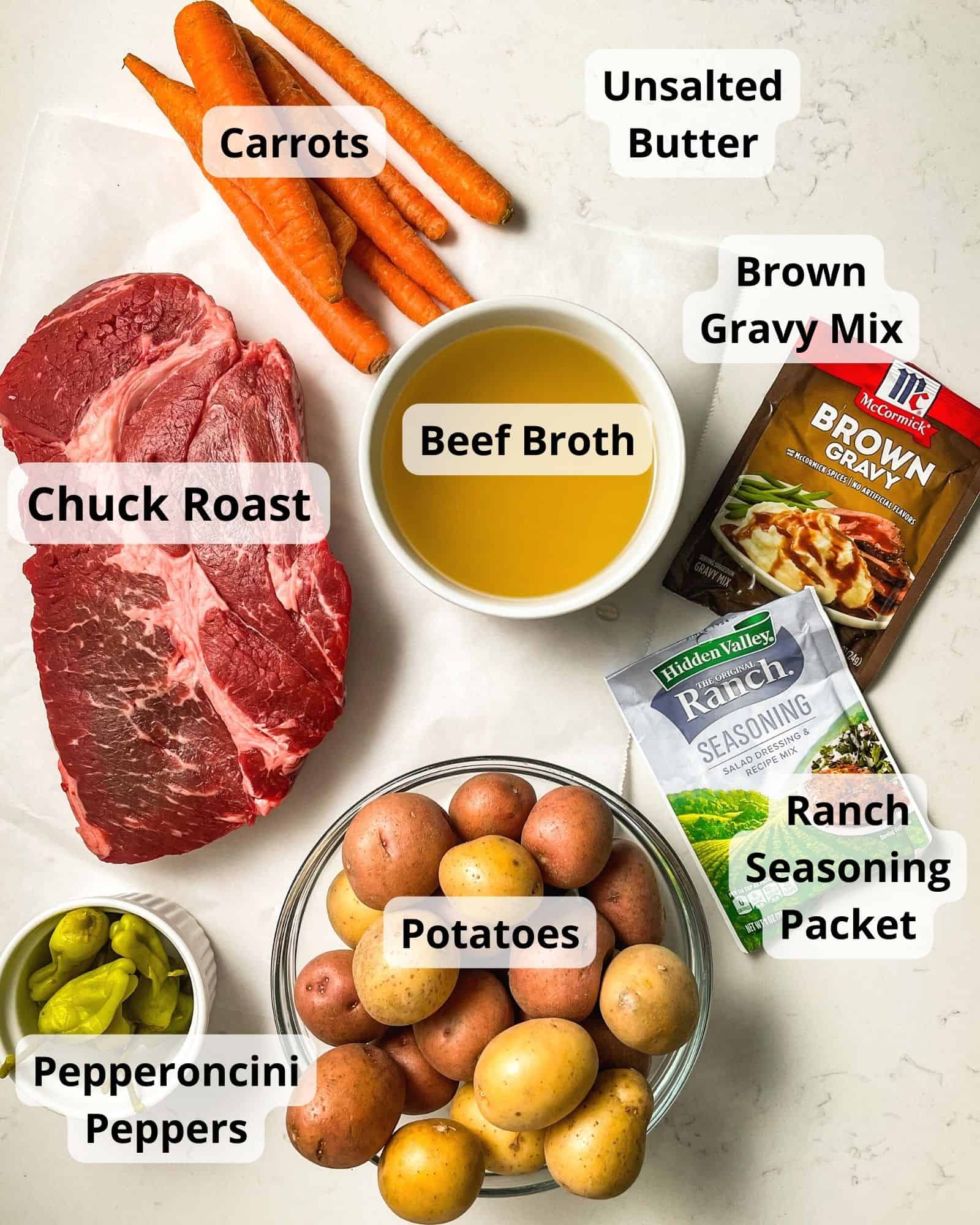 ingredients to make mississippi pot roast - chuck roast, beef broth, carrots, butter, brown gravy mix, ranch mix, pepperoncini peppers, and potatoes.
