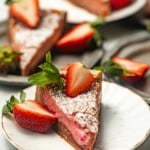 a slice of strawberry butter cake on a white plate with a sliced strawberry on top.