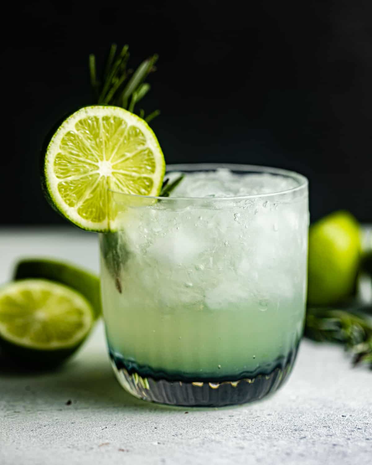 vodka gimlet on a grey surface garnished with a lime wheel and rosemary.