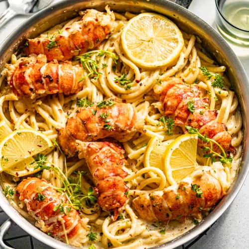 butter poached lobster on top of pasta in a pan with lemons and parsley.
