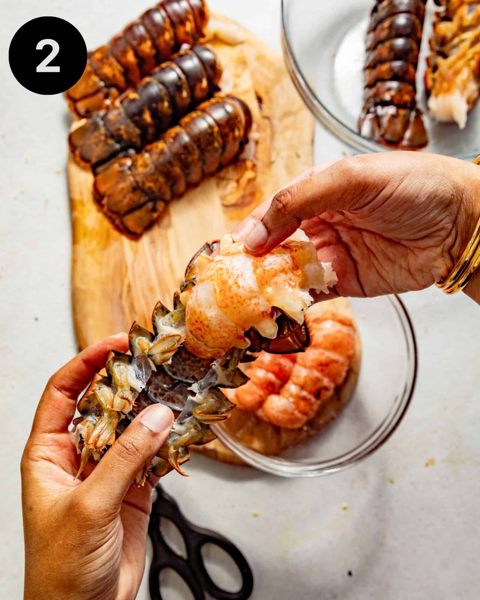 a cracked open lobster tail with hands pulling the lobster meat out.