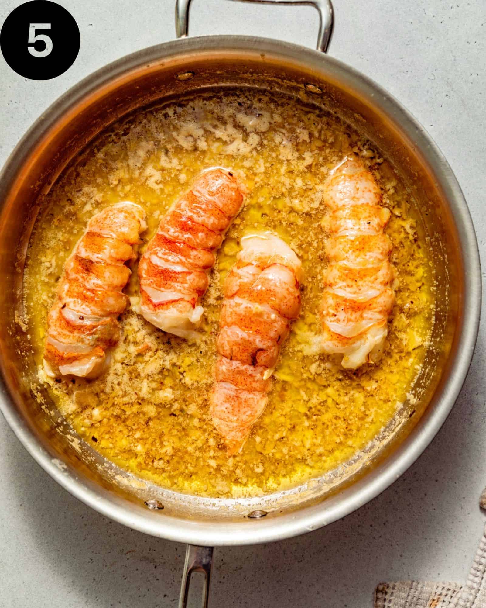 lobster tails poached in butter in a pan.