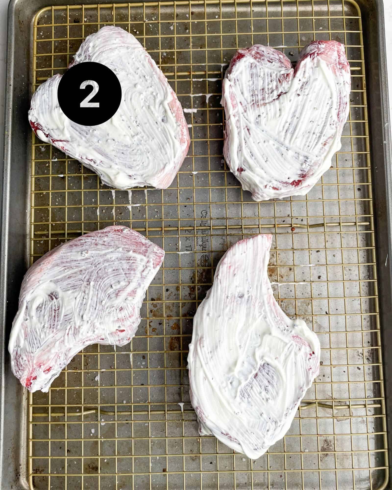 pork chops on a sheet pan with sour cream spread on top.