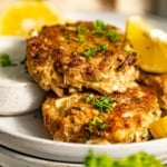 Pan fried crab cakes stacked on a dinner plate with lemon wedges.