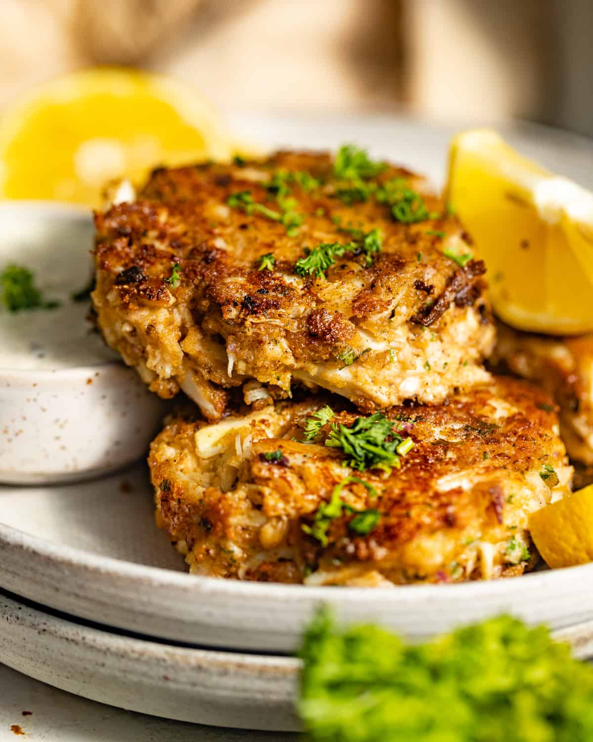 Pan fried crab cakes stacked on a dinner plate with lemon wedges.