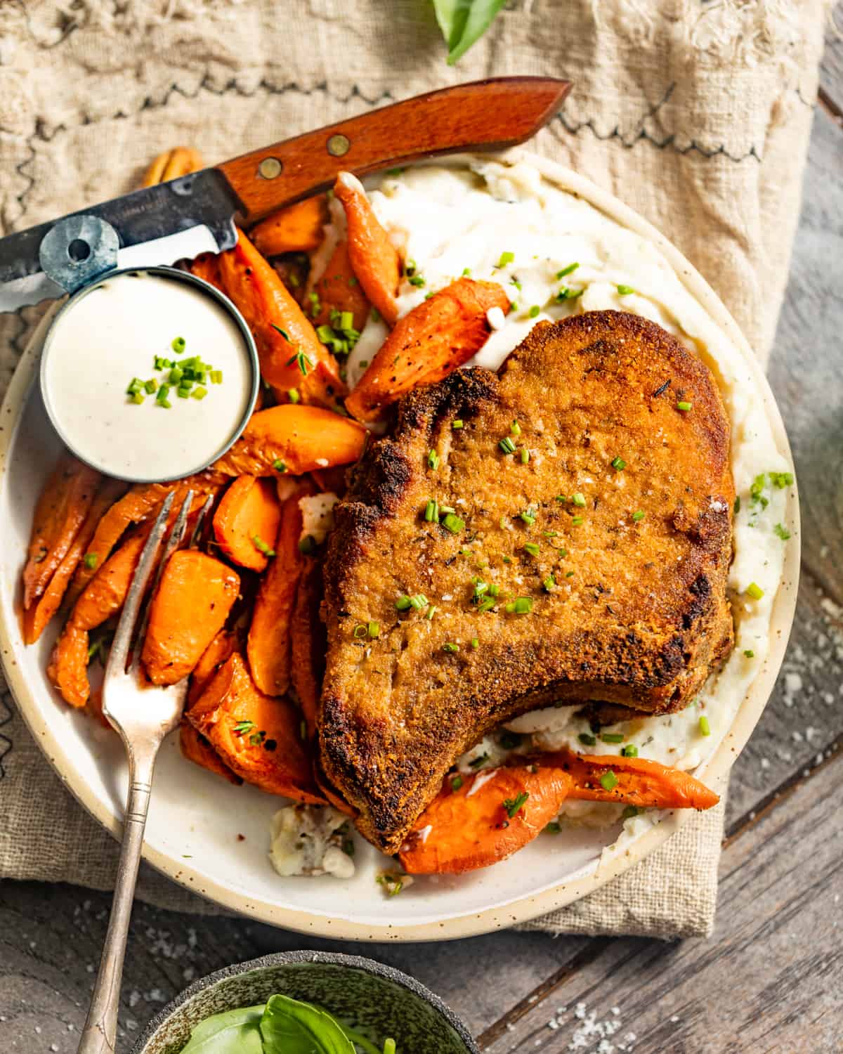 crispy baked pork chops on a plate with carrots and a fork and knife.