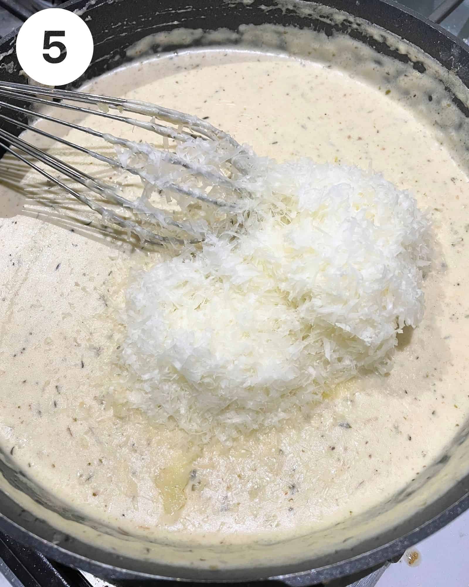 alfredo sauce in a pan with grated parmesan and asiago cheese on top.