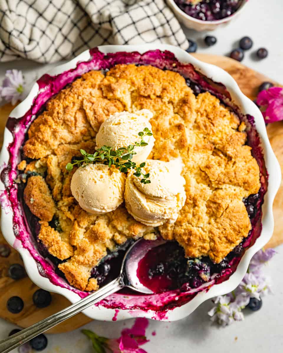 blueberry cobbler in a pie pan topped with vanilla ice cream.