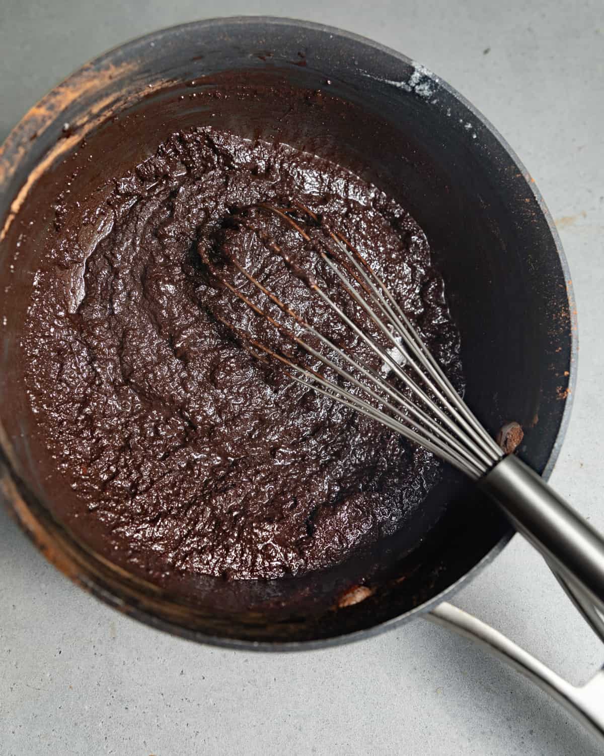 A whisk in a saucepan of brownie batter.