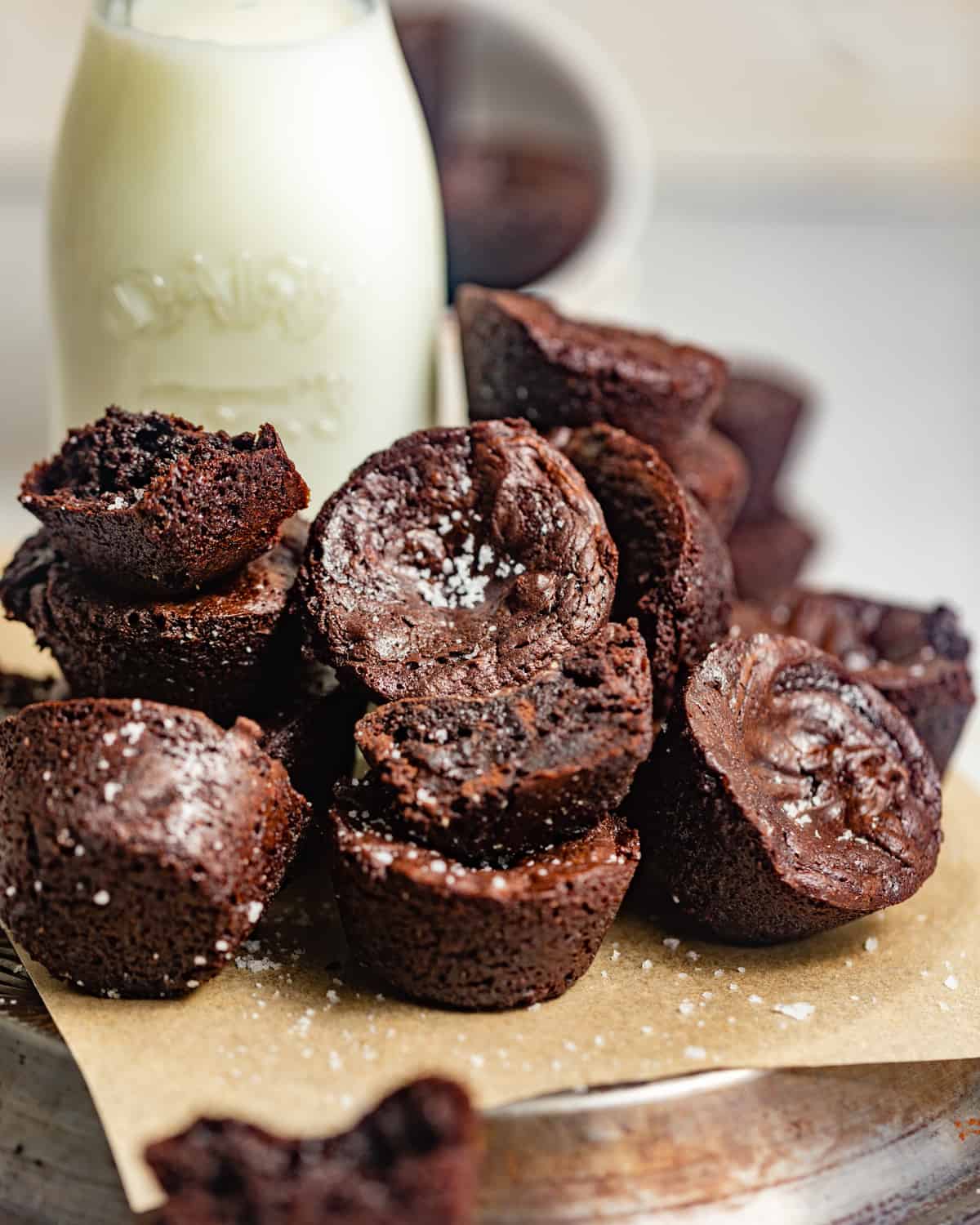 Mini brownie bites sprinkled with salt piled on a square of parchment paper in front of a jar of milk.