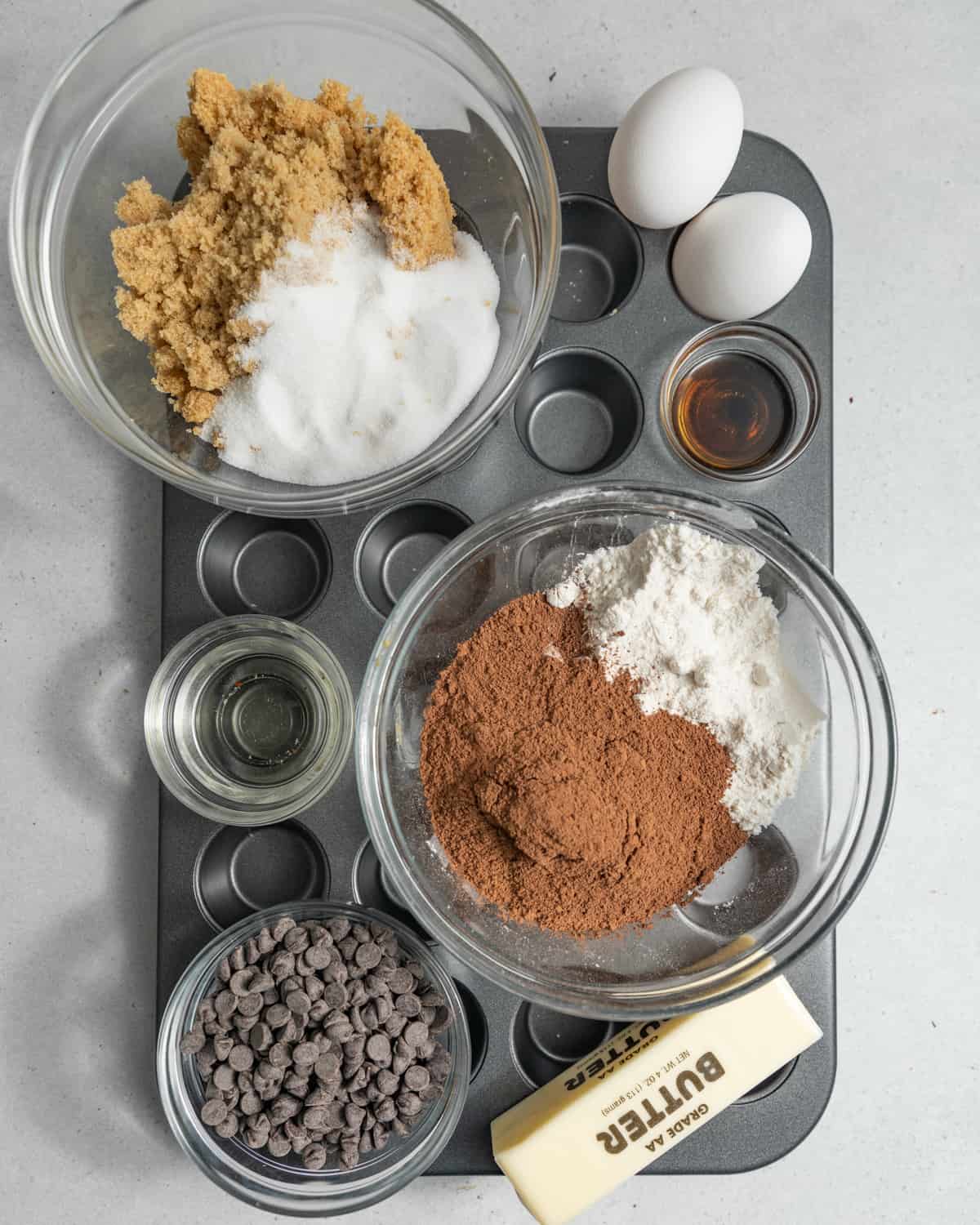 Ingredients for brownie bites in small bowls on top of a mini muffin tin.