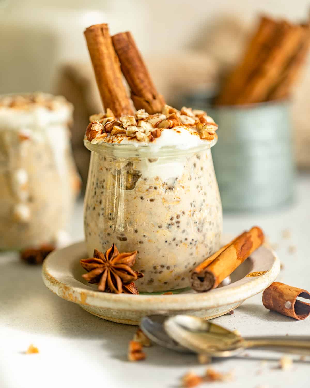 A small jar of cinnamon roll overnight oats next to whole spices on a table.