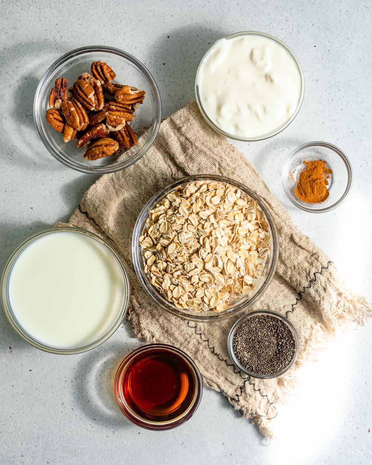 Ingredients to make cinnamon roll overnight oats in small bowls on a white surface.