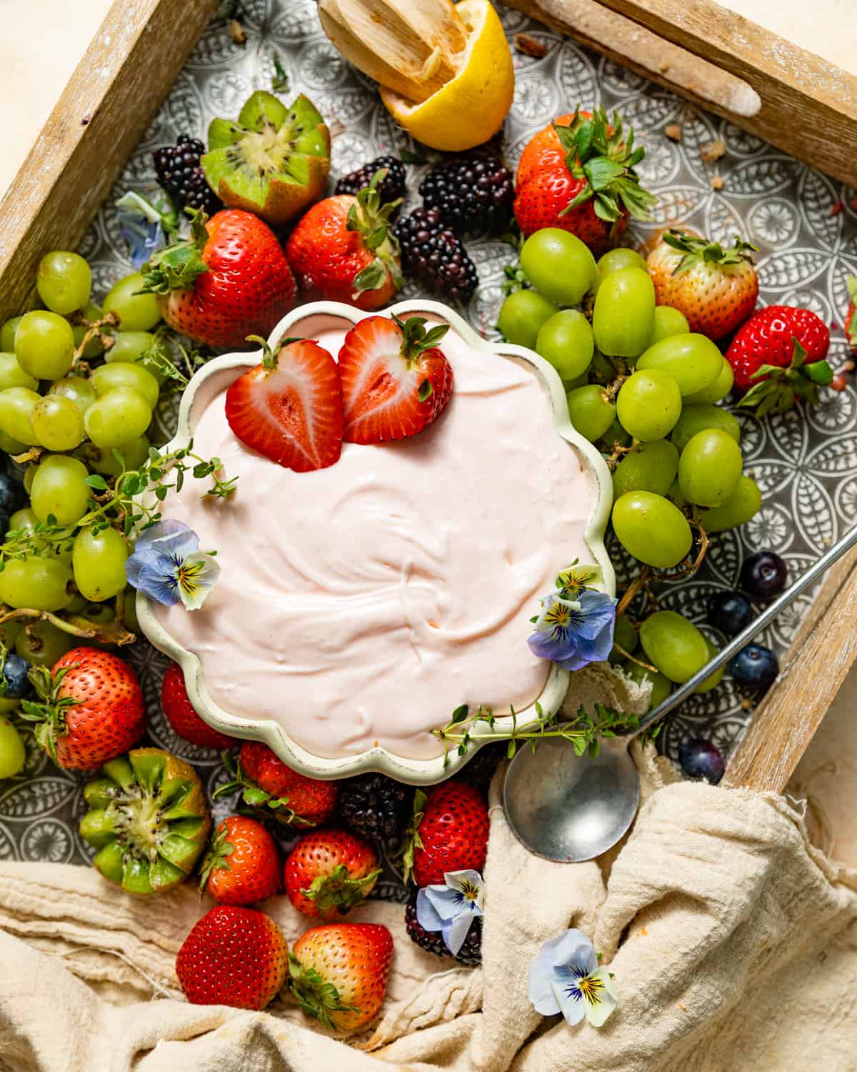 a fruit board with grapes and strawberries with a fruit dip in a bowl topped with edible flowers.