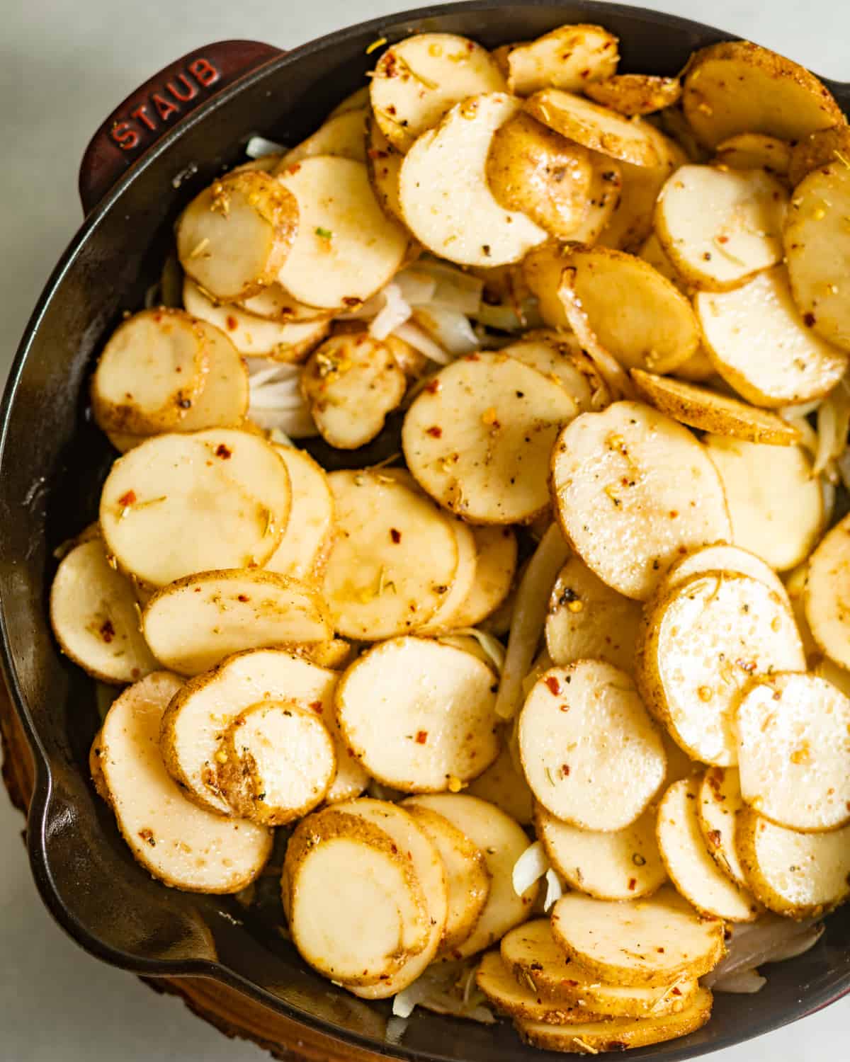 Sliced potatoes with seasonings placed in a cast iron skillet.