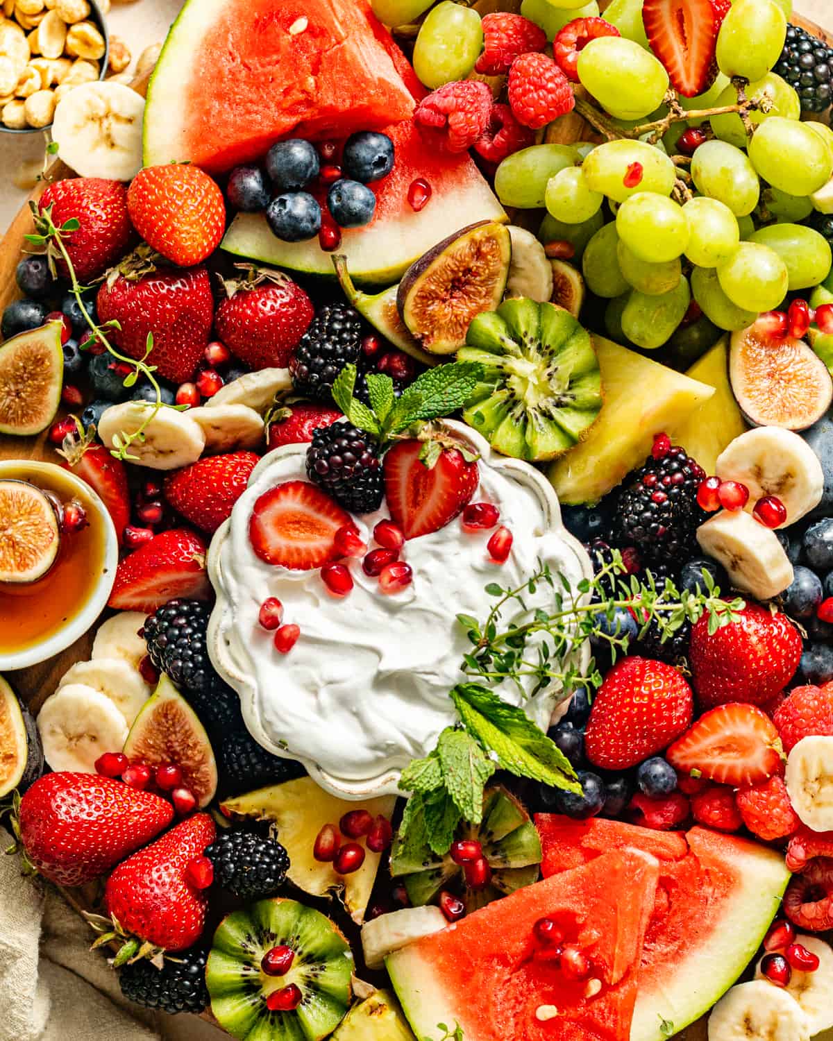 a variety of fruits on a fruit platter with dips in a bowl.