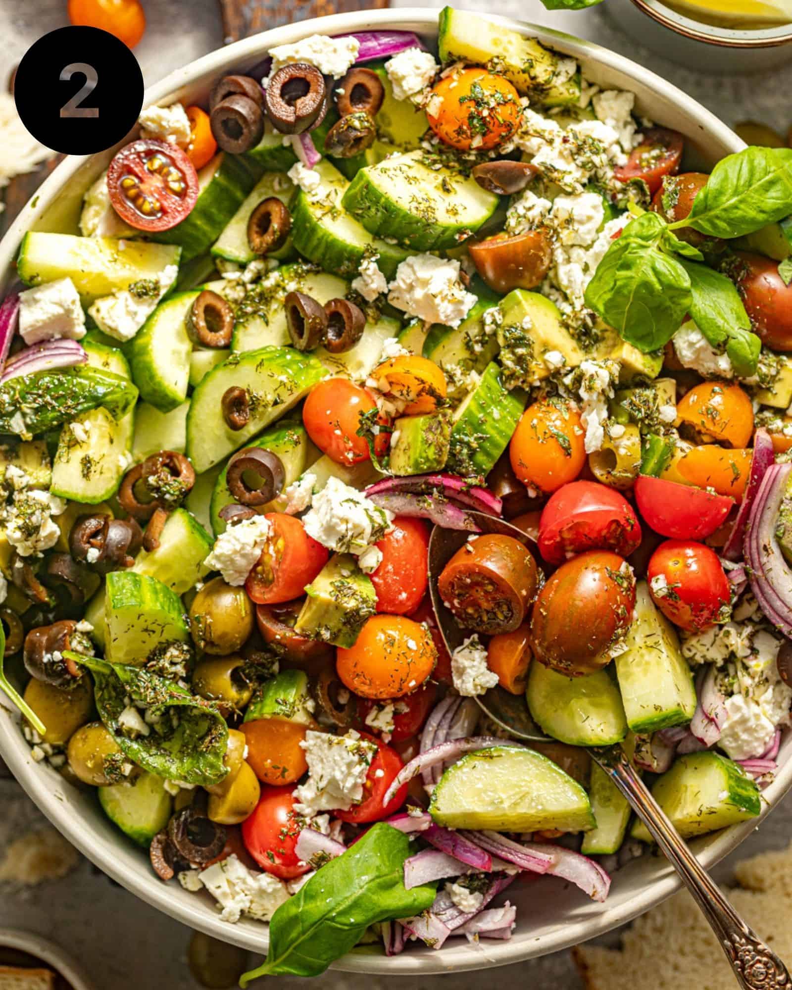 a large greek salad in a bowl garnished with fresh herbs and chopped tomatoes and feta.