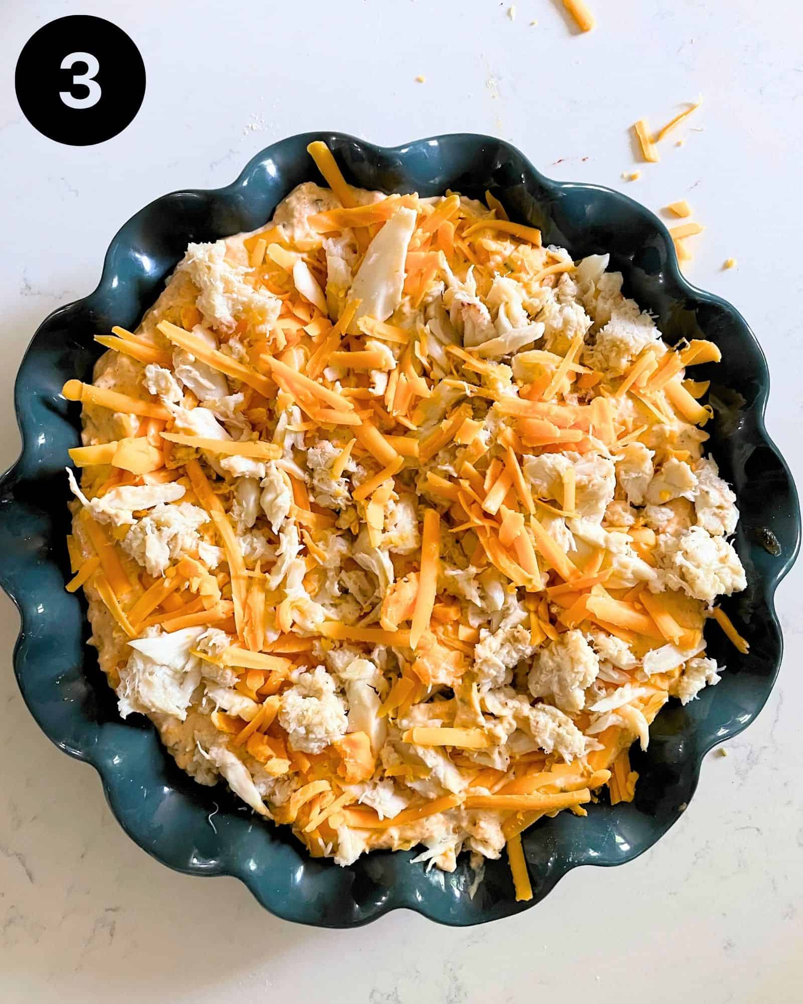 crab dip in a 9 inch baking dish with shredded cheese on top.