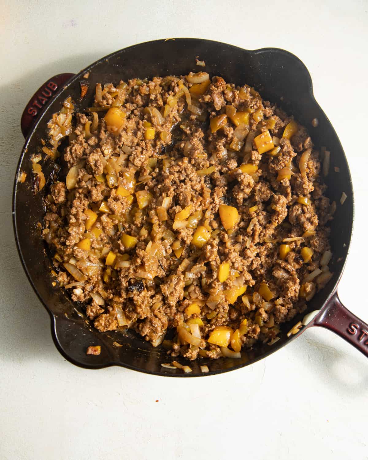 Browned ground beef with diced peppers and onions in a cast iron skillet.