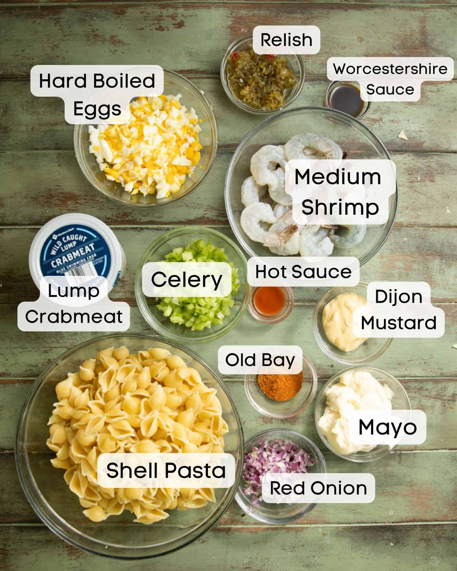 ingredients to make seafood pasta salad - crab meat, shrimp, celery, mayo, red onion, hot sauce, worcestershire sauce, dijon mustard, old bay seasoning, relish, and shell pasta.