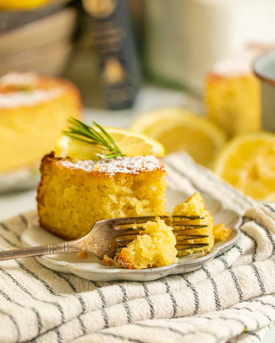 lemon rosemary olive oil cake with a piece taken out of it on a plate.