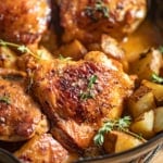 Maple dijon chicken thighs with chopped potatoes in a cast iron skillet.