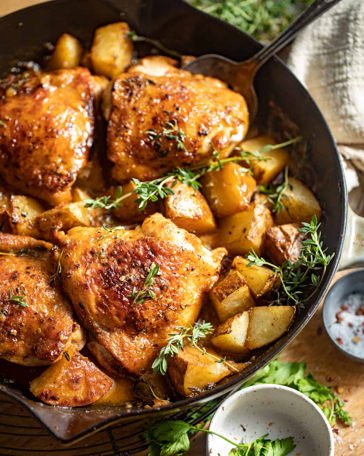 Maple dijon chicken thighs with chopped potatoes in a cast iron skillet.