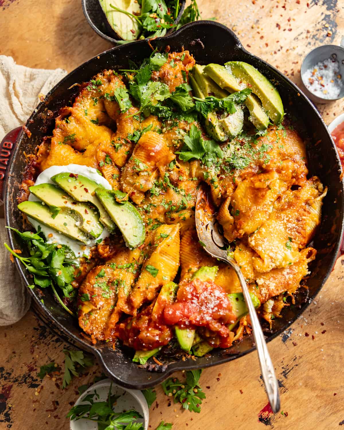 Cast iron skillet of Mexican stuffed shells topped with avocado and onion.