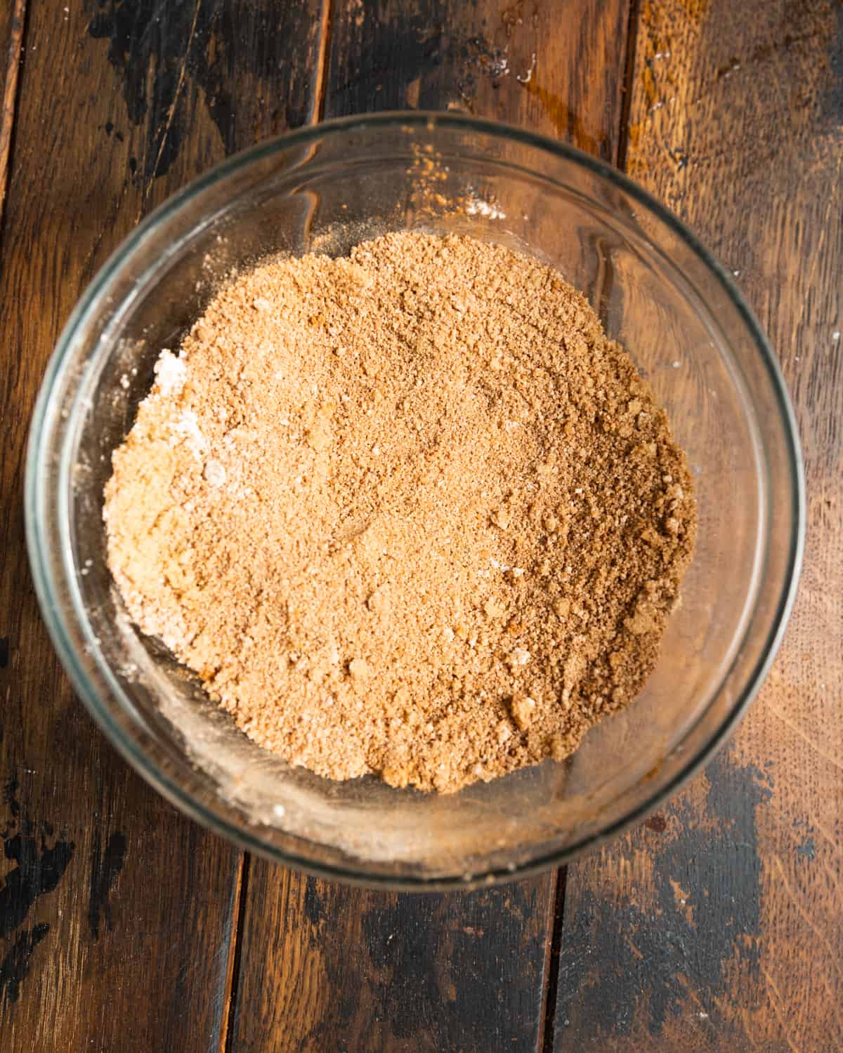Brown sugar and various spices in a small glass mixing bowl on a wooden table.