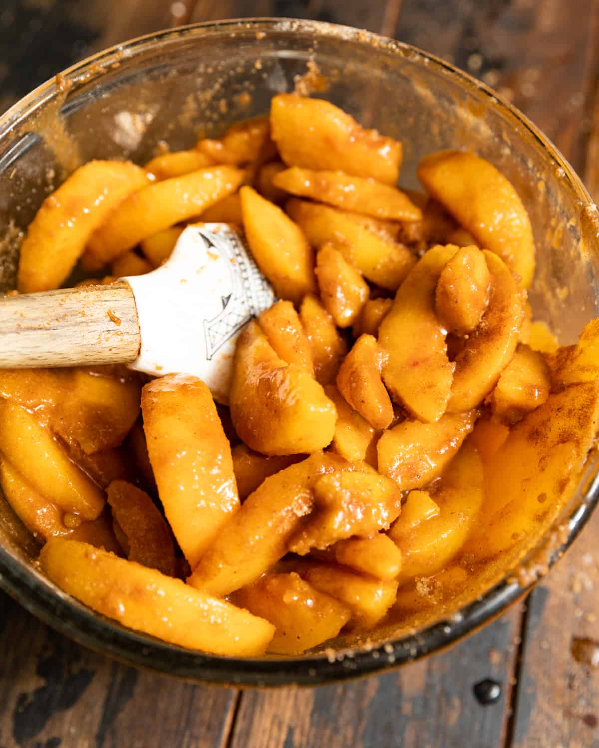 A rubber spatula in a mixing bowl of sugary peach slices.