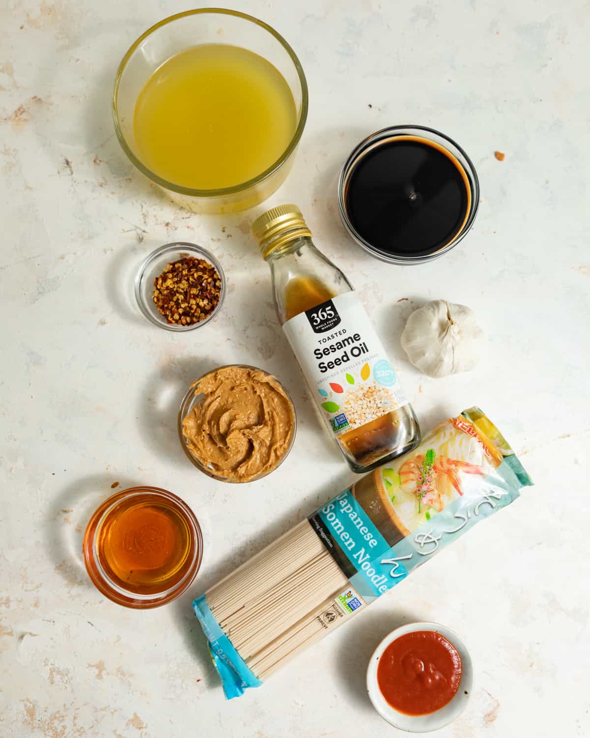 Ingredients to makes spicy peanut noodles on a white surface.