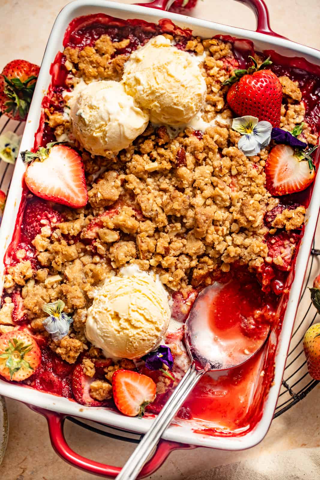 strawberry crisp in a baking dish with ice cream on top and a spoon.