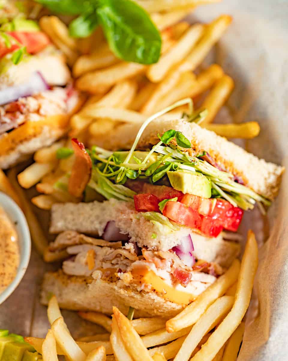 a club sandwich cut into a triangle and placed on a plate with french fries.