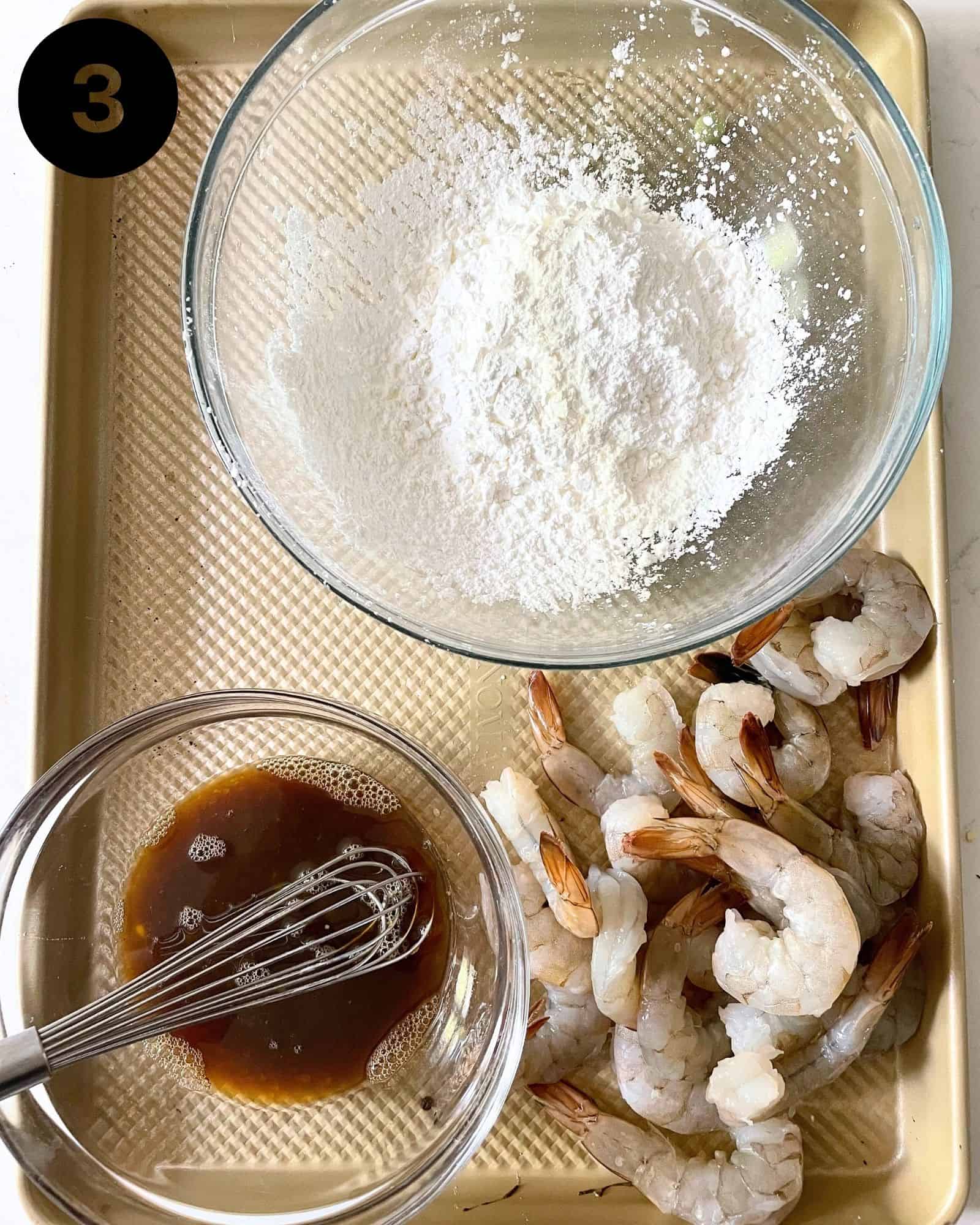 cornstarch in a bowl, shaoxing wine, soy sauce, and egg in a separate bowl, and shrimp on a baking sheet.
