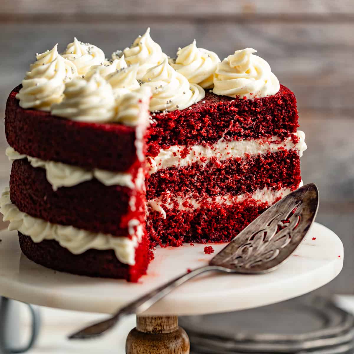 red velvet cake on a cake stand with a piece cut out showing the inner cake layers.