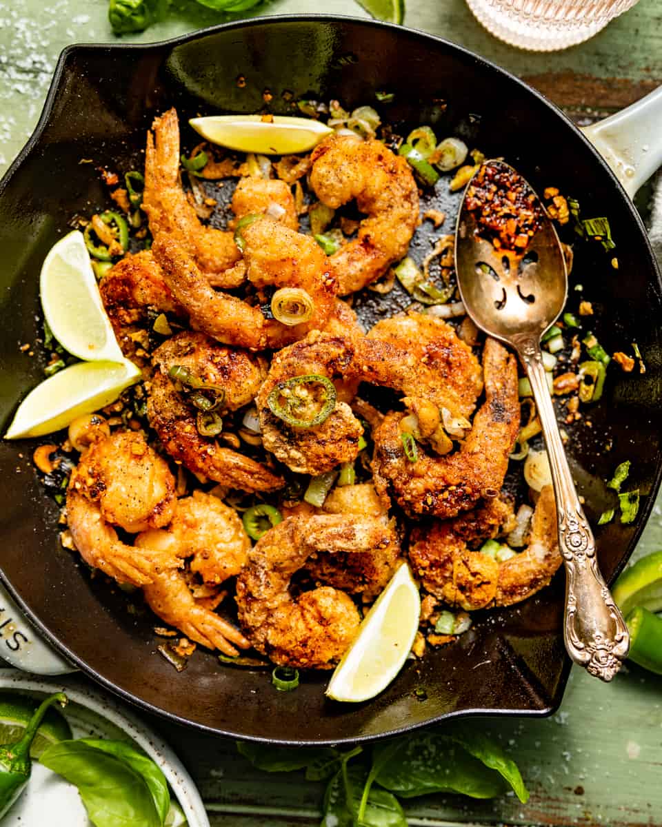 salt and pepper shrimp in a skillet with a spoon.