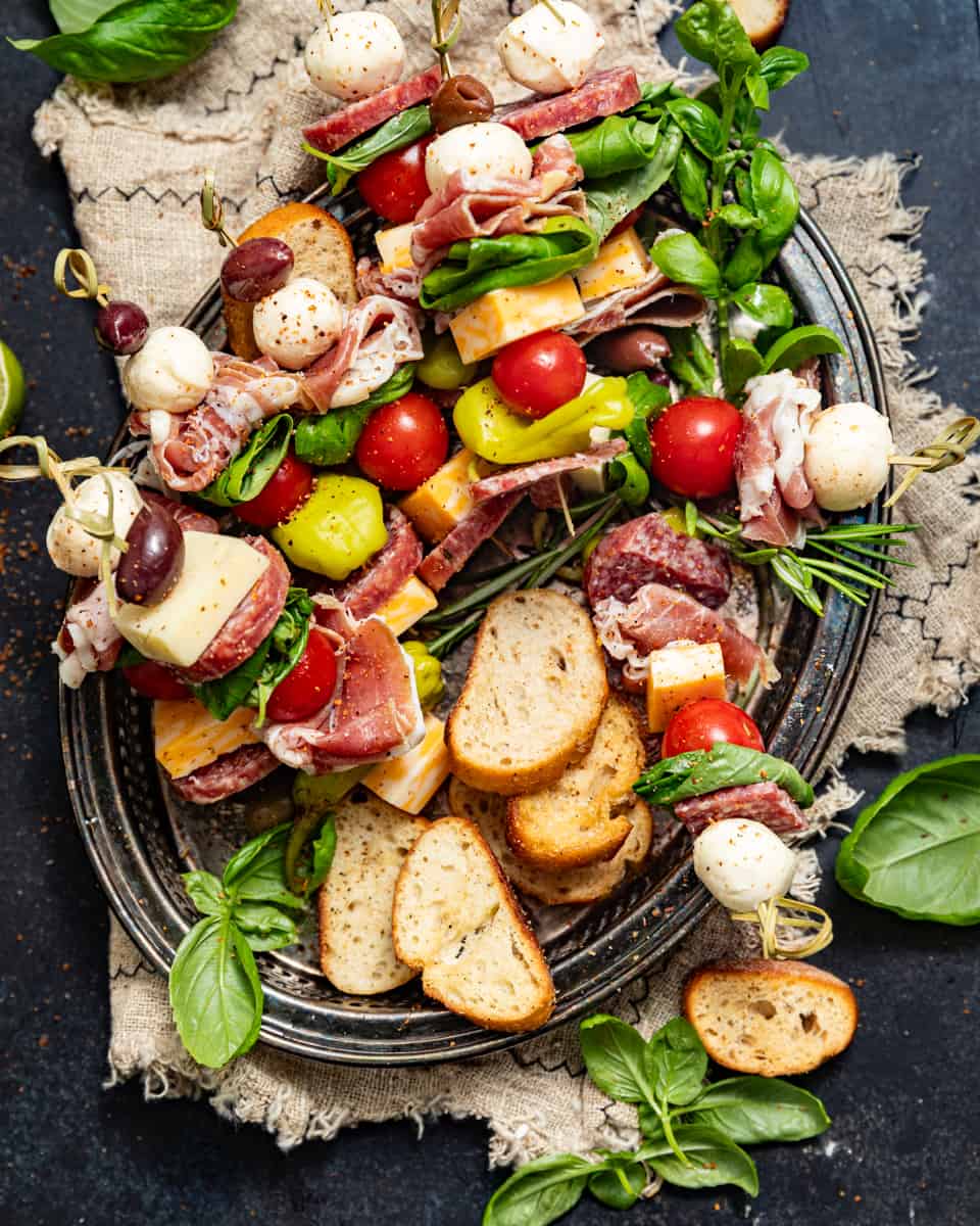 charcuterie skewers on a serving plate with crackers and fresh rosemary.