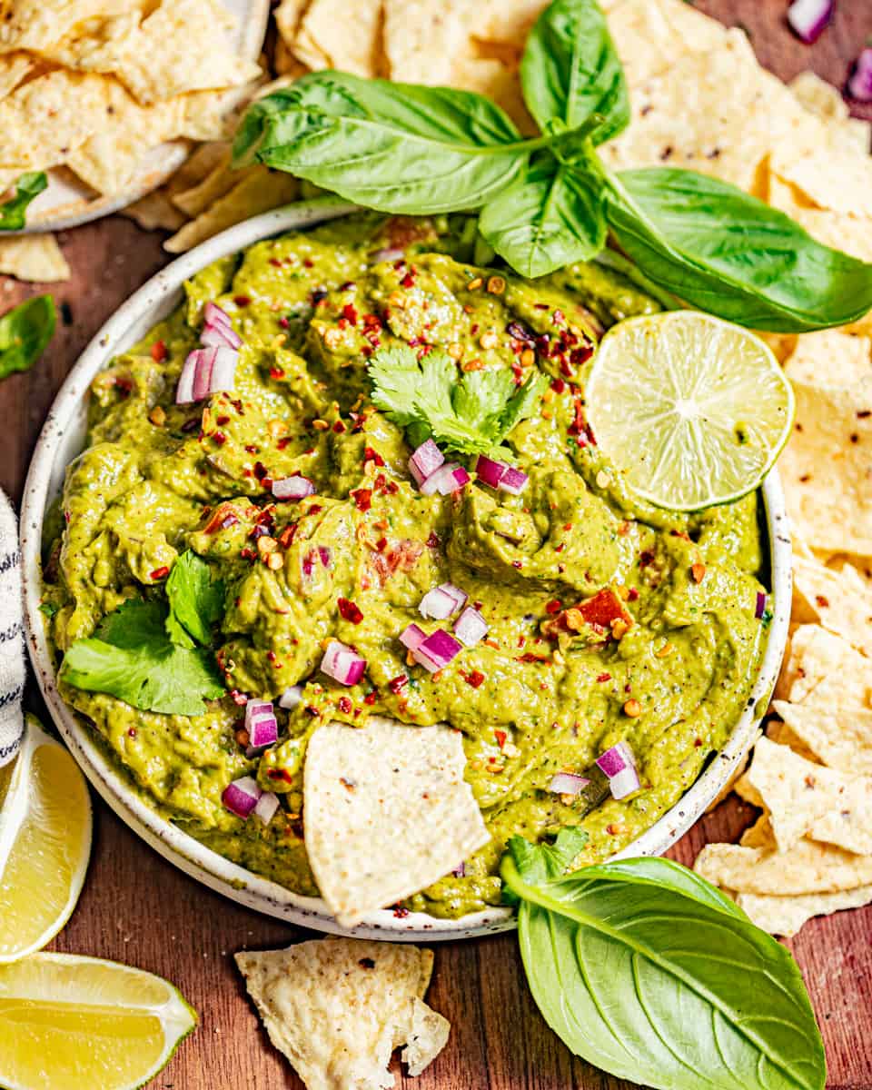 guacamole in a bowl on a serving board with tortilla chips and lime wedges.